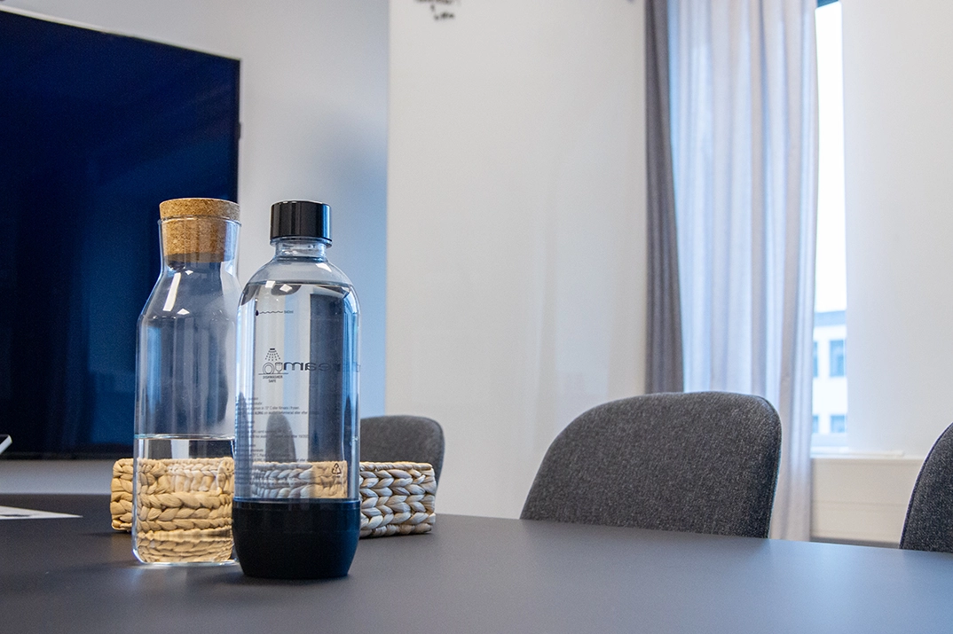Två vattenflaskor på ett mörkt bord i en kontorsmiljö eller mötesrum.