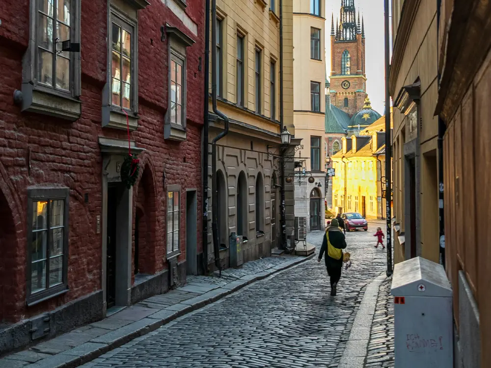En kvinna som går på en liten gata i Stockholm med färgglada byggnader runt henne.
