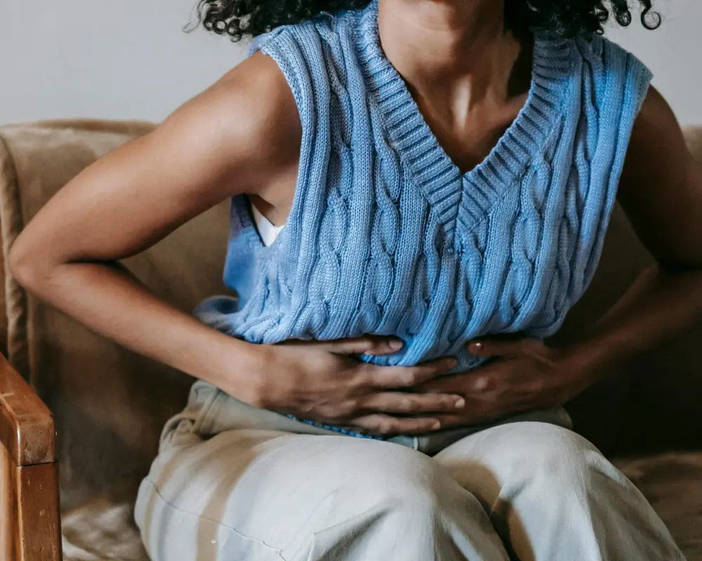 En kvinna som sitter ner på en soffa och har ont i magen.