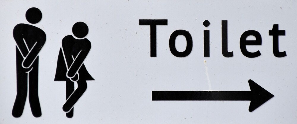 En rolig toalettskylt med manliga och kvinnliga symboler som pekar riktning utomhus